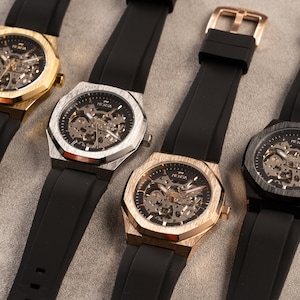 May include: Four wristwatches with black rubber bands and octagonal faces. The faces are skeletonized and have a gold, silver, or black finish.
