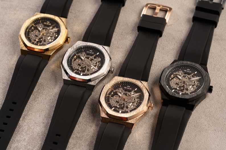 May include: Four wristwatches with black rubber bands and octagonal faces. The faces are skeletonized and have a gold, silver, or black finish.