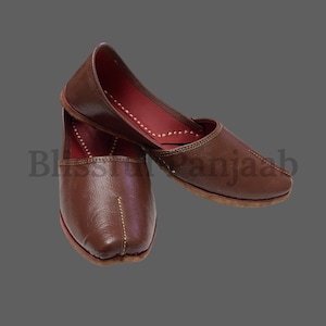 Puede incluir: Un par de zapatos de cuero marrón con punteras puntiagudas y un detalle de costura decorativo. Los zapatos tienen un forro de cuero rojo y están hechos en un estilo tradicional.