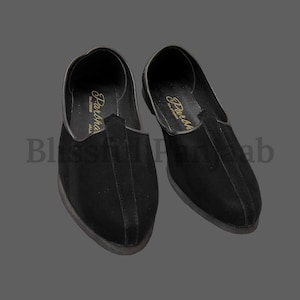 Puede incluir: Un par de zapatos de cuero negro con punta puntiaguda y un detalle de costura decorativa. Los zapatos tienen una etiqueta dorada con el texto "Pakha" en el zapato izquierdo y "Durba" en el zapato derecho.