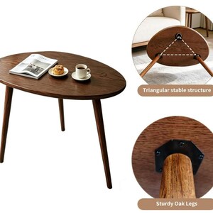 Puede incluir: Una mesa auxiliar de madera marr&oacute;n oscuro con tablero ovalado y tres patas c&oacute;nicas. La mesa presenta una estructura triangular estable y patas de roble resistentes fijadas con herrajes met&aacute;licos negros. Un libro, un pastel y una taza encima.