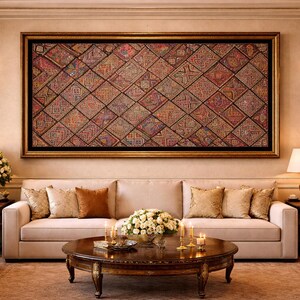 Puede incluir: Un lujoso salón con una gran obra de arte textil enmarcada con un patrón geométrico en tonos rojos, marrones y dorados. La habitación incluye dos sofás color crema, una mesa de centro redonda y cojines decorativos. Arreglos florales y apliques de pared realzan el ambiente elegante.