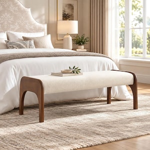 May include: A rectangular bench featuring a cream-colored upholstered seat and a dark brown wooden frame with curved legs. A small book and a decorative green plant sprig are placed on the center of the bench seat.