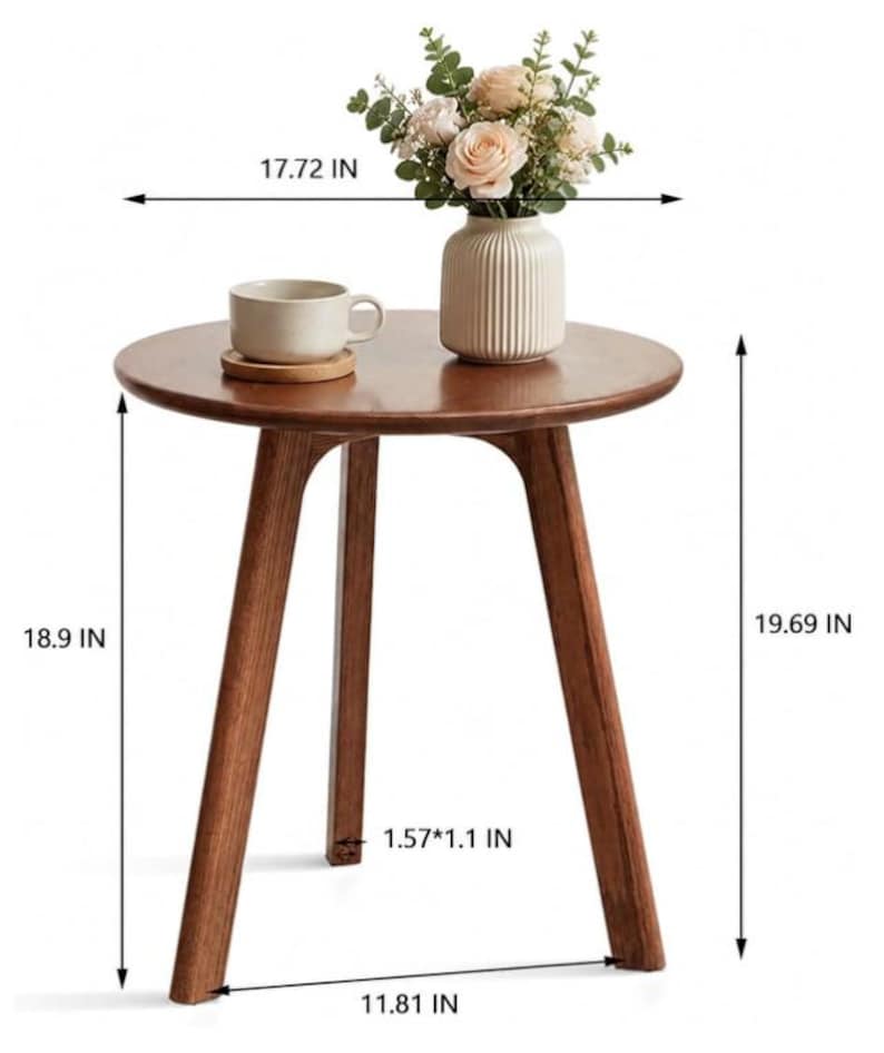 Puede incluir: Una mesa auxiliar redonda de madera con tres patas inclinadas, que mide 45 cm de di&aacute;metro y 50 cm de altura. La mesa tiene un acabado marr&oacute;n claro y sostiene un jarr&oacute;n de cer&aacute;mica beige con flores y una taza beige sobre un posavasos.