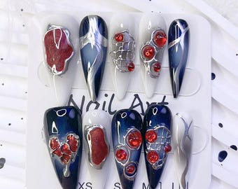 May include: Set of ten false nails with different designs. Each nail is painted with a blue and white ombre effect and decorated with red and silver accents. The nails are arranged on a white card with the words "Nail Art" printed on it.