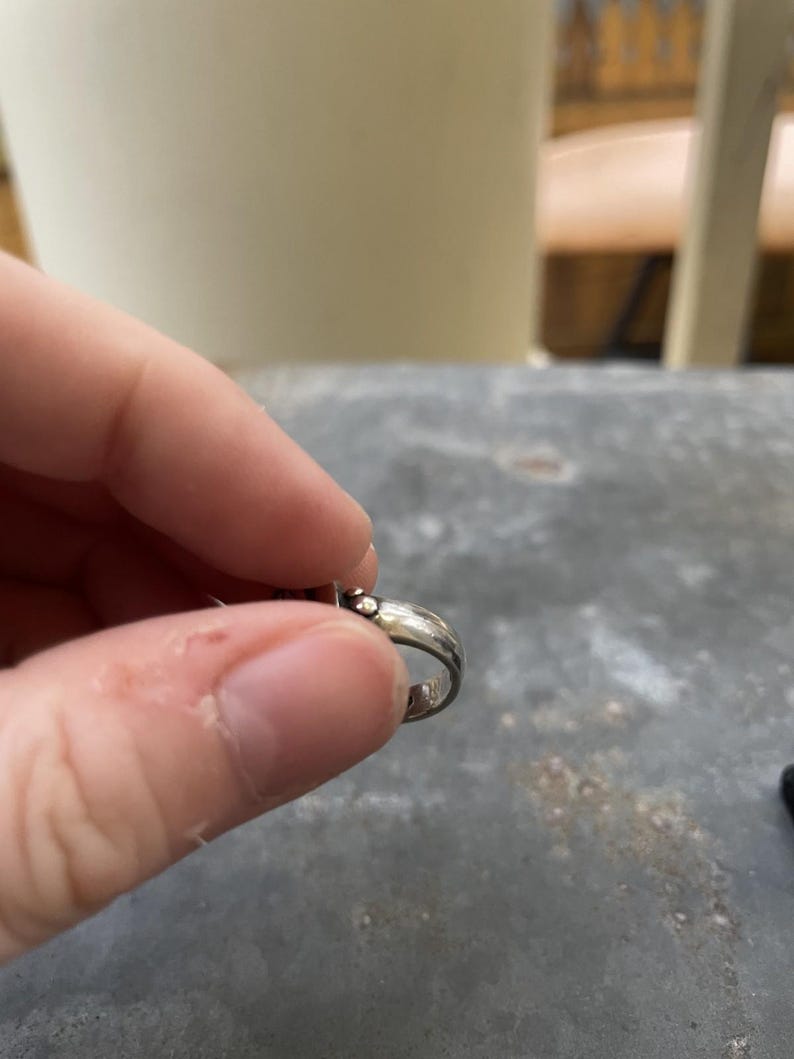 Puede incluir: Una taza de cer&aacute;mica blanca con un asa negra y el texto "But First, Coffee" en negrita negra. La taza se encuentra sobre un fondo borroso, sugiriendo un ambiente acogedor.