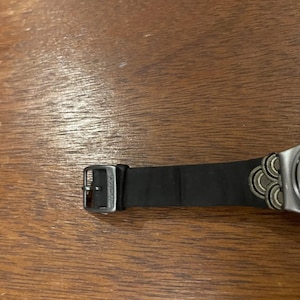 Op de afbeelding: Een witte keramische mok met een zwart handvat en de tekst "But First, Coffee" in een zwarte, vette letter. De mok staat op een houten oppervlak. De mok is ongeveer 10 cm hoog.