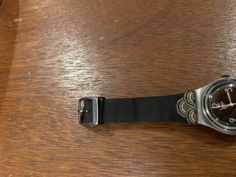 Op de afbeelding: Een witte keramische mok met een zwart handvat en de tekst "But First, Coffee" in een zwarte, vette letter. De mok staat op een houten oppervlak. De mok is ongeveer 10 cm hoog.