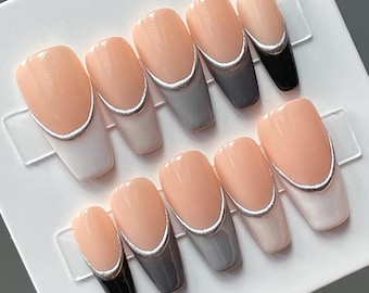 Puede incluir: Un conjunto de diez uñas postizas en una variedad de colores. Las uñas presentan una base de color melocotón claro con un borde metálico plateado. Algunas uñas tienen puntas blancas, grises o negras. Las uñas están dispuestas en un soporte de plástico transparente.