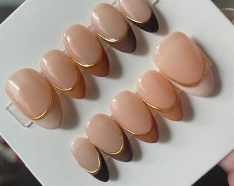 May include: Set of ten nude-colored false nails with a gold accent and brown and black tips.