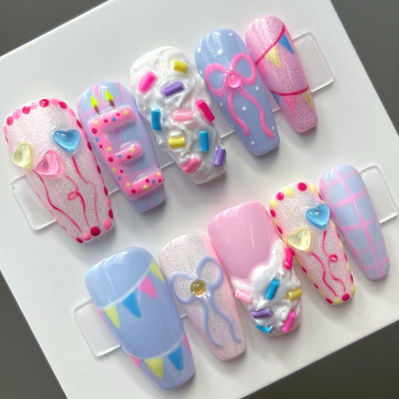 May include: A set of ten press-on nails featuring pastel colors, glitter finishes, and 3D embellishments. Designs include raised bows, textured frosting with colorful sprinkles, heart-shaped gems, birthday candles, and festive bunting patterns.