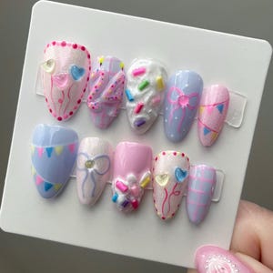 May include: A set of ten almond-shaped press-on nails featuring a birthday theme. Designs include pink and blue plaid, white frosting with colorful sprinkles, light blue with bunting, pink with bows, and heart balloons with the number 24.