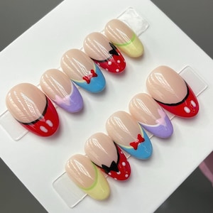May include: Set of ten false nails with a Disney theme. The nails are oval shaped and feature a variety of colors and designs, including red, blue, yellow, purple, and white. Each nail has a different design, including Mickey Mouse, Minnie Mouse, and Donald Duck.