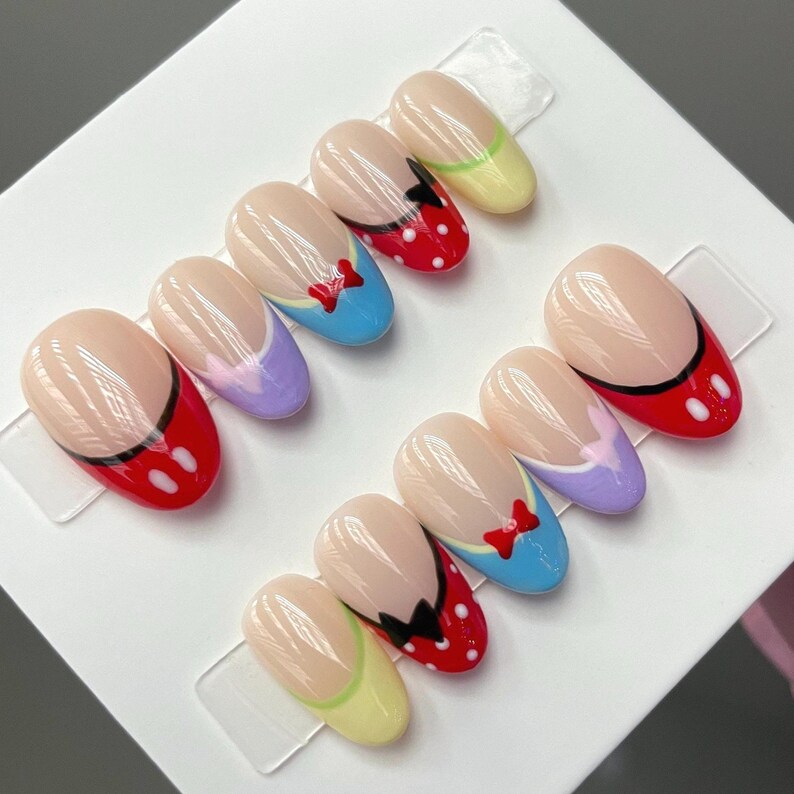 May include: Set of ten false nails with a Disney theme. The nails are oval shaped and feature a variety of colors and designs, including red, blue, yellow, purple, and white. Each nail has a different design, including Mickey Mouse, Minnie Mouse, and Donald Duck.