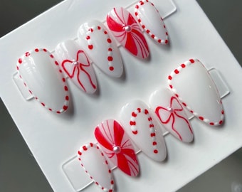 Puede incluir: Conjunto de seis uñas postizas blancas con diseños de bastón de caramelo y lazo rojos y blancos.