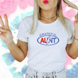 May include: White t-shirt with a blue and red oval graphic that says "Grateful Aunt" with a lightning bolt in the middle.