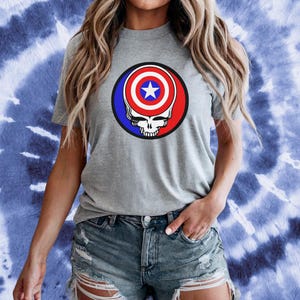 Puede incluir: Camiseta gris con un gr&aacute;fico rojo, blanco y azul de una calavera con el escudo del Capit&aacute;n Am&eacute;rica como cabeza.