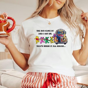 May include: White t-shirt with a colorful graphic of a bus with dancing bears and the text "THE BUS CAME BY AND I GOT ON. THAT'S WHEN IT ALL BEGAN..."