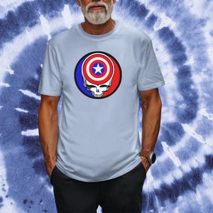 Puede incluir: Una camiseta azul claro con un gr&aacute;fico de una calavera con el escudo del Capit&aacute;n Am&eacute;rica como cabeza. El escudo es rojo, blanco y azul.