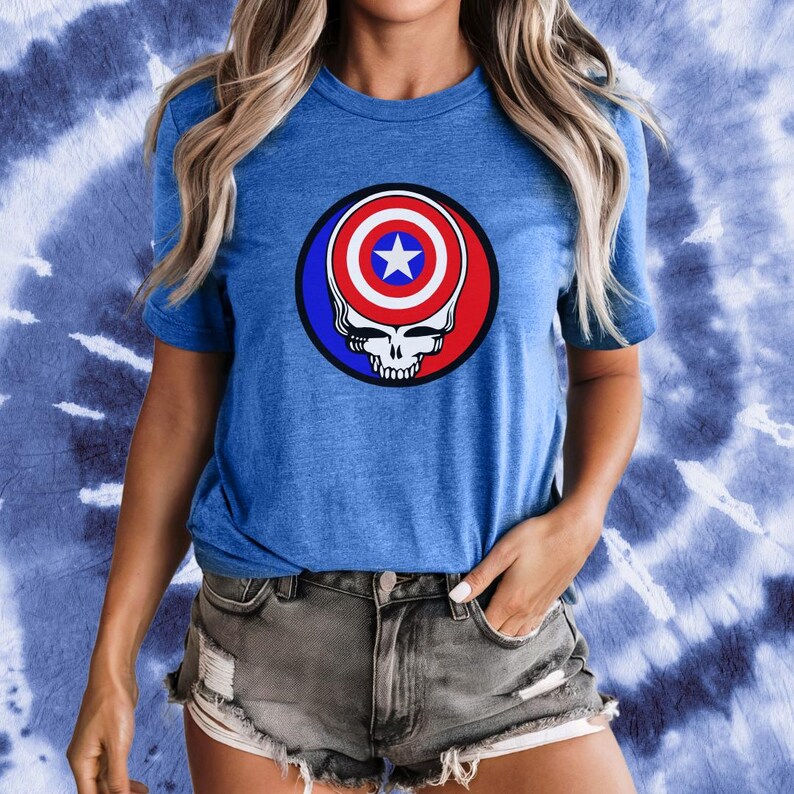 Puede incluir: Una camiseta azul con un gr&aacute;fico rojo, blanco y azul de una calavera con el escudo del Capit&aacute;n Am&eacute;rica como cabeza de la calavera.