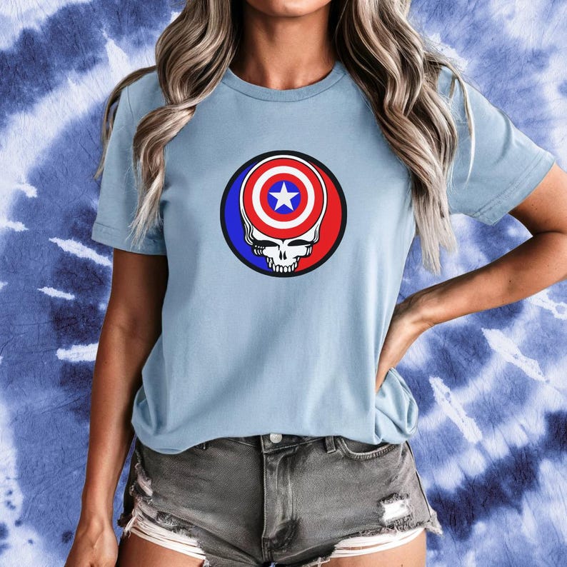 Puede incluir: Una camiseta azul claro con un gr&aacute;fico de una calavera con una bandera estadounidense roja, blanca y azul en su interior. La calavera est&aacute; rodeada por un c&iacute;rculo azul.