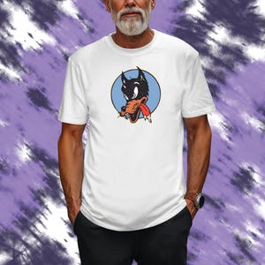 May include: White t-shirt featuring a cartoon wolf head with a red tongue, black fur, and a light blue circle background. The wolf graphic is centered on the shirt. The shirt is short-sleeved.