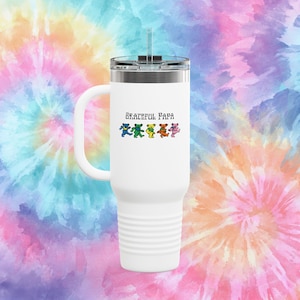 May include: A white travel mug with a handle and a silver lid. The mug features the text "Grateful Papa" above a row of colorful dancing bears. The background is a tie-dye pattern in shades of blue, pink, orange, and yellow.
