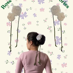 May include: A person wearing a pink long-sleeved shirt and blue jeans with two white crocheted rose hair accessories. The background is a light yellow with a pattern of pink and purple bows and green leaves.
