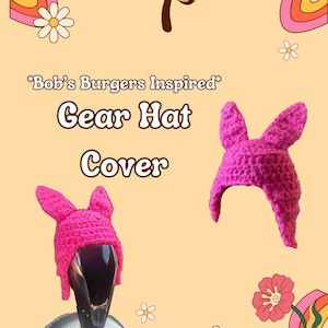 Op de afbeelding: Een felroze gehaakte versnellingspookhoes, geïnspireerd op Bob's Burgers, met lange konijnenoren. De afbeelding bevat de tekst "Bob's Burgers Inspired" en "Gear Hat Cover" in een retro lettertype, met bloemen en regenboogdecoraties.