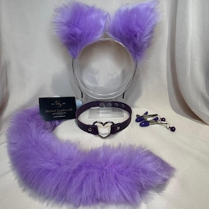 Op de afbeelding: Een set paarse nepbont kattenoren, -staart en een donkerpaarse choker met een hartvormige hanger. Inclusief tepelklemmen met paarse kralen. Er is ook een visitekaartje aanwezig.