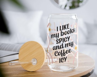 May include: A clear glass can-shaped tumbler with a bamboo lid and straw. The tumbler has the text "I LIKE my books SPICY and my Coffee ICY" in black and pink. The tumbler sits on a wooden table.
