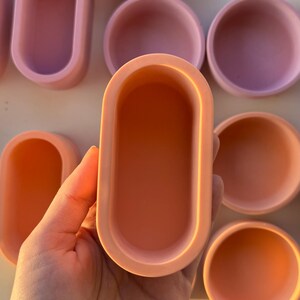 Peut inclure: Collection de petits contenants en céramique de couleur pastel. L'image présente des plateaux ovales et des bols ronds dans des tons de rose et de pêche. Ces contenants faits à la main sont probablement destinés aux bijoux ou aux petits objets.
