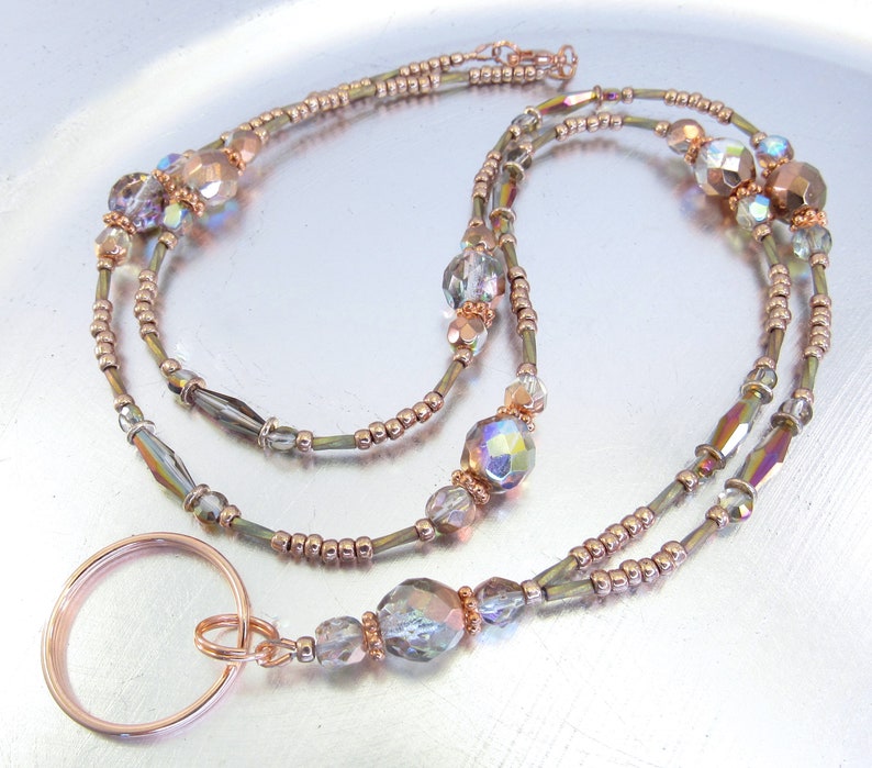 Puede incluir: Un cord&oacute;n con cuentas con cuentas iridiscentes y oro rosa. El cord&oacute;n tiene un gran anillo de oro rosa en la parte inferior y est&aacute; dise&ntilde;ado con m&uacute;ltiples hilos de cuentas. Las cuentas son una mezcla de formas redondas y facetadas.