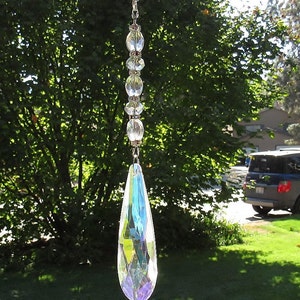 May include: A crystal suncatcher with a teardrop-shaped prism hanging from a chain of clear beads. The suncatcher is iridescent and reflects light.