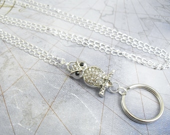 May include: A silver chain with a rhinestone owl charm and a silver ring attached. The owl has black eyes.