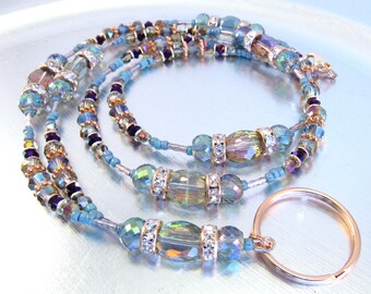 May include: A multi-strand beaded lanyard with blue, gold, and purple beads. The lanyard has a gold metal ring attached to the end.