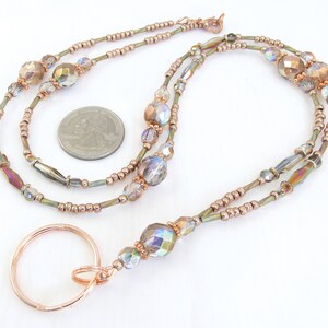 Puede incluir: Un cord&oacute;n con cuentas con un llavero de color cobre. El cord&oacute;n presenta cuentas iridiscentes y facetadas y cuentas m&aacute;s peque&ntilde;as de color cobre ensartadas en un cord&oacute;n fino de color verde oliva. El llavero es de metal color cobre.