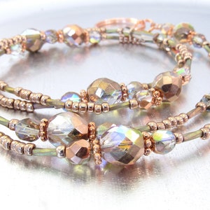 Puede incluir: Collar de m&uacute;ltiples hilos con cuentas facetadas iridiscentes y cuentas de color cobre. El collar tiene un dise&ntilde;o delicado y elegante con una mezcla de cuentas transparentes e iridiscentes, creando un efecto brillante. La joya se exhibe sobre una superficie plateada.