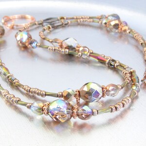 Puede incluir: Un delicado collar con cuentas de cristal iridiscentes y cuentas m&aacute;s peque&ntilde;as en tono dorado. El collar tiene un dise&ntilde;o de doble hebra con un cierre y detalles en color cobre. Las cuentas reflejan m&uacute;ltiples colores, creando un efecto brillante.