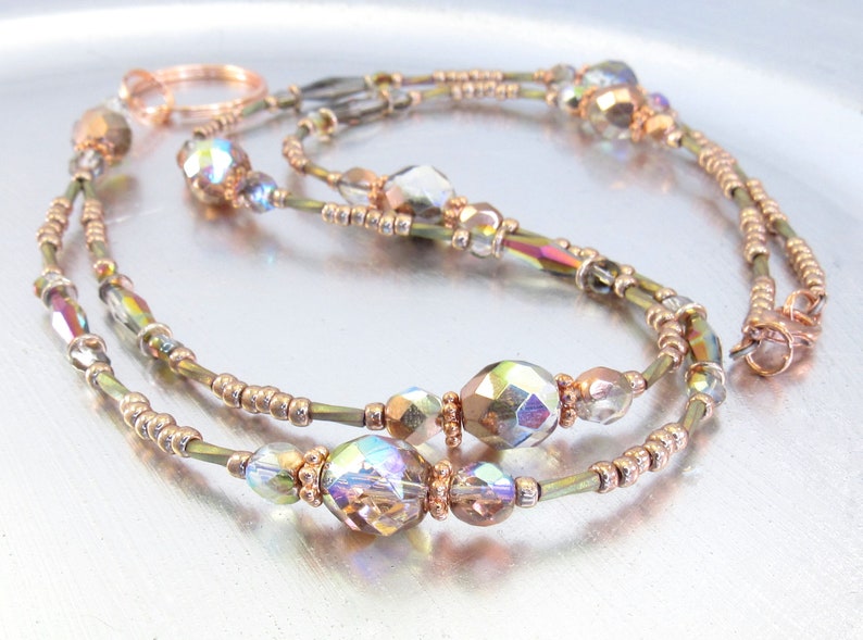 Puede incluir: Un delicado collar con cuentas de cristal iridiscentes y cuentas m&aacute;s peque&ntilde;as en tono dorado. El collar tiene un dise&ntilde;o de doble hebra con un cierre y detalles en color cobre. Las cuentas reflejan m&uacute;ltiples colores, creando un efecto brillante.