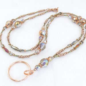 Puede incluir: Un cord&oacute;n con cuentas con un llavero de color cobre. El cord&oacute;n presenta cuentas iridiscentes y facetadas y cuentas m&aacute;s peque&ntilde;as de color cobre ensartadas en un alambre fino de color verde oliva. El cord&oacute;n est&aacute; dise&ntilde;ado para usarse alrededor del cuello.