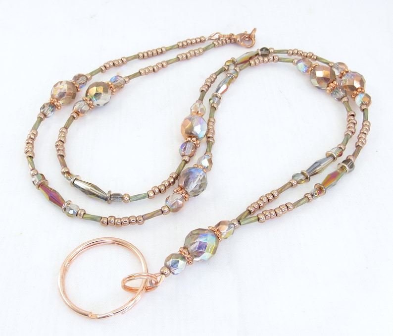 Puede incluir: Un cord&oacute;n con cuentas con un llavero de color cobre. El cord&oacute;n presenta cuentas iridiscentes y facetadas y cuentas m&aacute;s peque&ntilde;as de color cobre ensartadas en un alambre fino de color verde oliva. El cord&oacute;n est&aacute; dise&ntilde;ado para usarse alrededor del cuello.