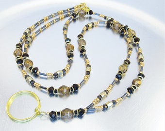 May include: A gold beaded lanyard with black and brown beads. The lanyard has a gold ring at the end.
