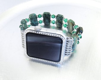 May include: A silver Apple Watch with a green and silver beaded band. The watch face is surrounded by a row of clear rhinestones.