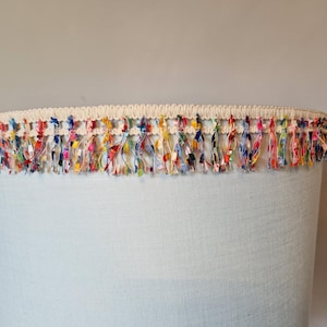May include: A light blue lampshade with a white trim and a colourful fringe around the top.