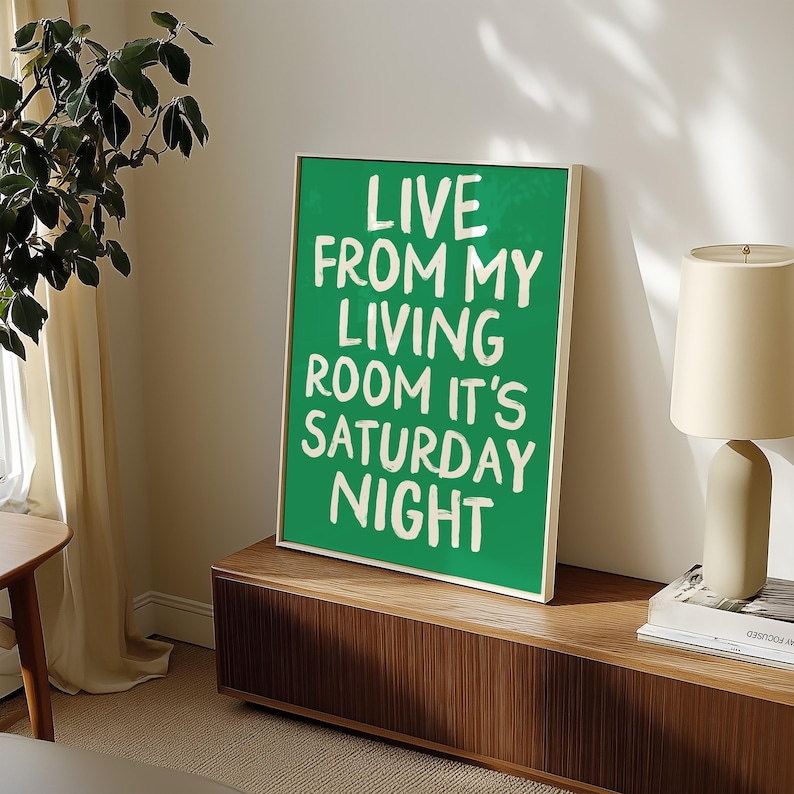 May include: A green framed poster with white text that reads "Live from my living room it's Saturday night". The poster is hanging on a wall above a wooden shelf.