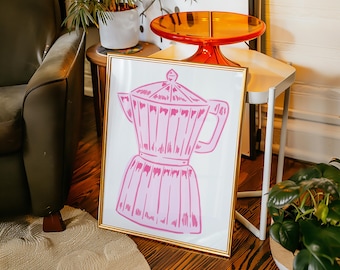 May include: A pink and white illustration of a coffee pot in a gold frame. The coffee pot is a traditional Italian design with a rounded body and a spout.