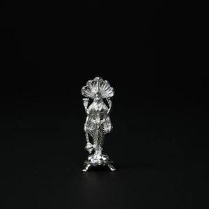May include: A detailed silver figurine of a deity, standing on a decorative base. The figure has an elaborate headdress and holds objects in its hands. The statue is set against a black background.