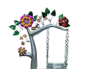 May include: A decorative metal tree sculpture with a swing. The tree features colorful flowers in shades of pink, yellow, and red, with green leaves. The swing is suspended by chains.