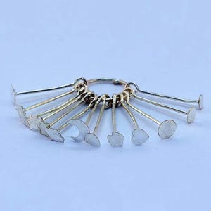 May include: A silver-toned charm ring with various small charms attached. The charms include shapes like clouds, moons, hearts, and circles. The ring and charms are made of a shiny metal.